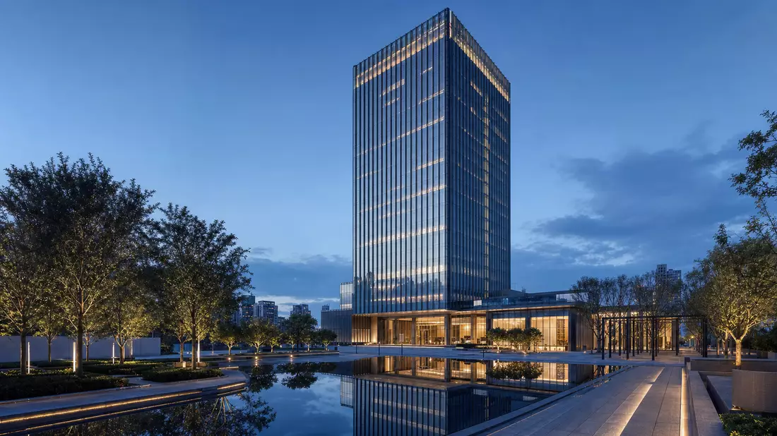 Architekturvisualisierung eines gläsernen Hochhauses mit Spiegelteich bei Dämmerung