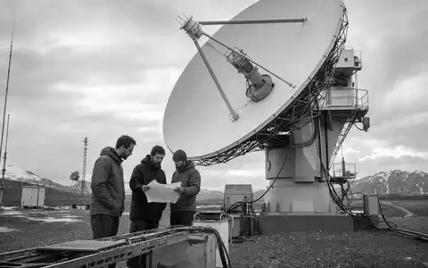 Schwarzweiss-Reportage dokumentiert fuer Leidos Holdings ISIN US5253271028 eine Satellitenanlage mit Ingenieuren im freien Gelaende - Foto: THN