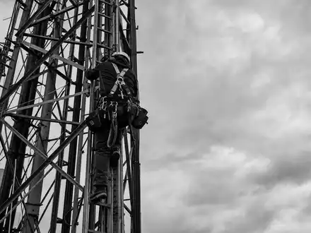 Schwarzweiß-Reportagefoto eines Technikers am Mast steht sinnbildlich für Cellnex Telecom S.A., ISIN ES0105066007, Turminfrastruktur-Wartung - Foto: THN
