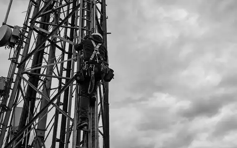 SchwarzweiĂ-Reportagefoto eines Technikers am Mast steht sinnbildlich fĂŒr Cellnex Telecom S.A., ISIN ES0105066007, Turminfrastruktur-Wartung - Foto: THN