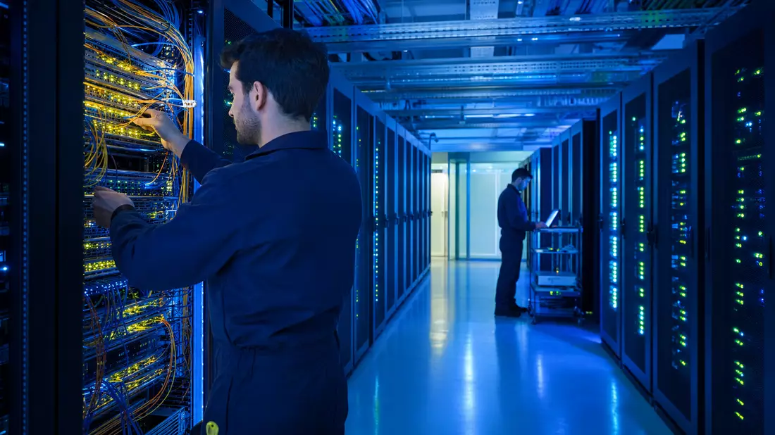 Techniker prüfen Glasfaser-Serverracks in einem modernen Rechenzentrum bei Nacht