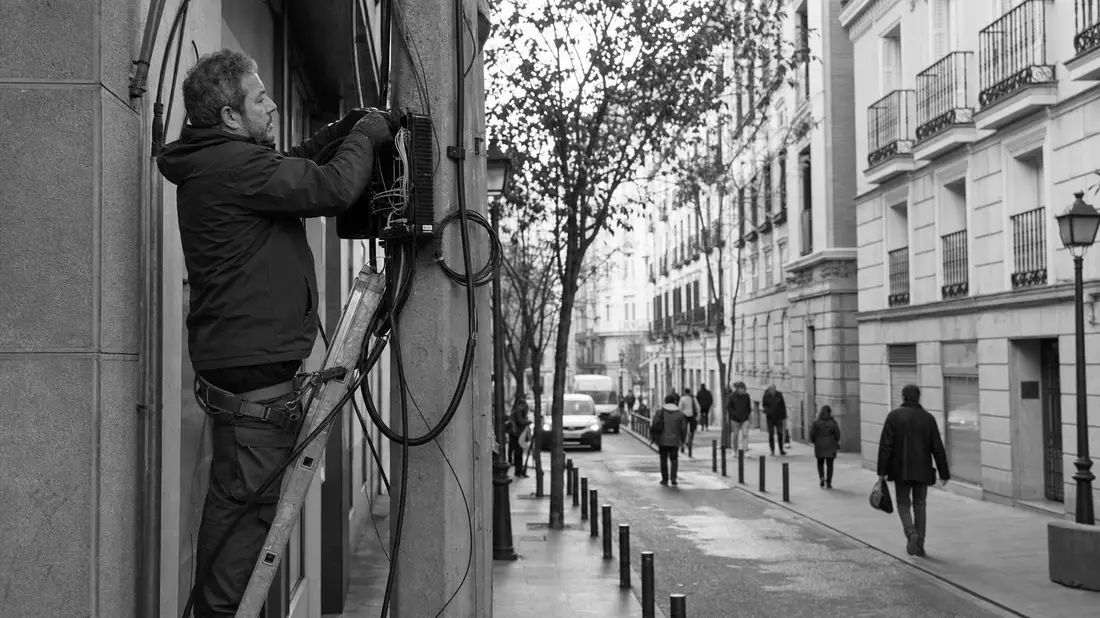 Schwarzweißfoto eines Technikers bei Glasfaser-Installation an Hausfassade in Madrid