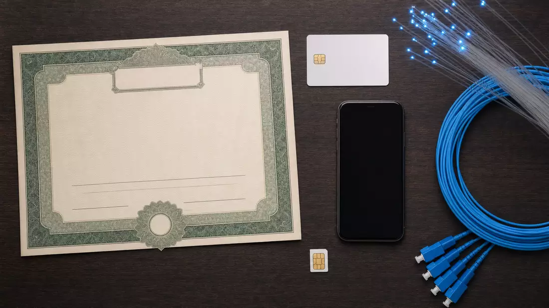 Flatlay mit Aktienzertifikat, ISIN-Karte, Smartphone und Glasfaserkabeln auf Holztisch
