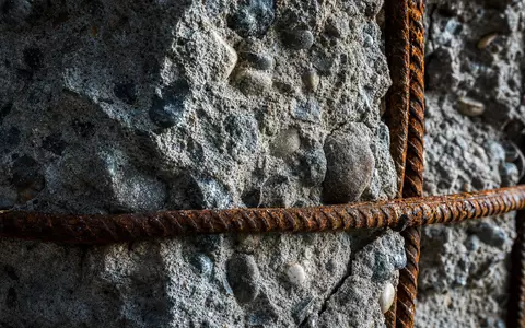 Bouygues S.A. FR0000120503 zeigt detailreiche Makroaufnahme von rohem Beton mit verrostetem Stahlbewehrungsgeflecht im Nahfokus - Foto: THN