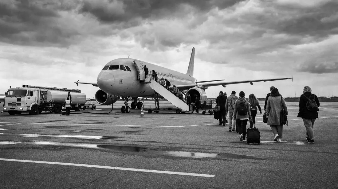 Schwarzweißfoto von Passagieren, die über das Rollfeld zu einem Flugzeug gehen