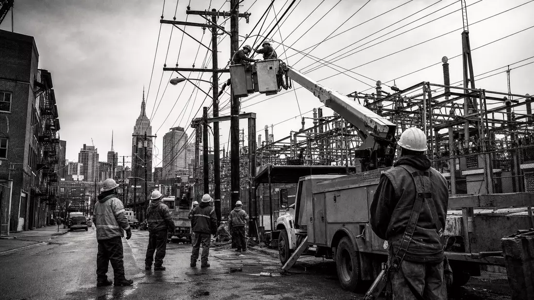 Schwarzweiß-Reportage: Elektriker in Hubwagen bei Leitungsarbeiten, NYC-Skyline