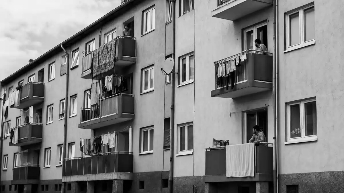 Schwarzweiß-Reportagefoto einer Wohnhausfassade mit Balkonen und Bewohnern
