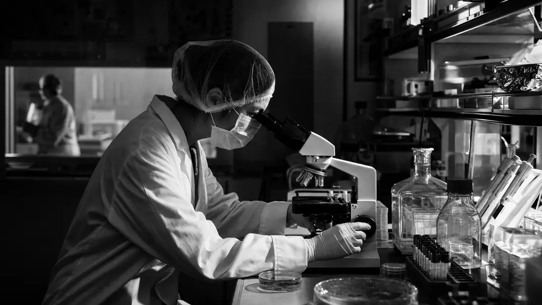 Schwarzweiß-Reportage: Gilead Sciences Forscherin am Mikroskop im Biopharma-Labor