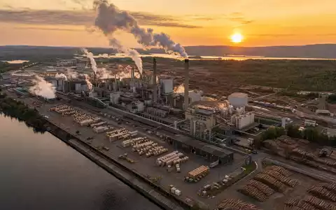 International Paper Zellstoffwerk US4601461035 bei goldenem Sonnenuntergang mit Holzlager und weißen Dampfwolken - Foto: THN