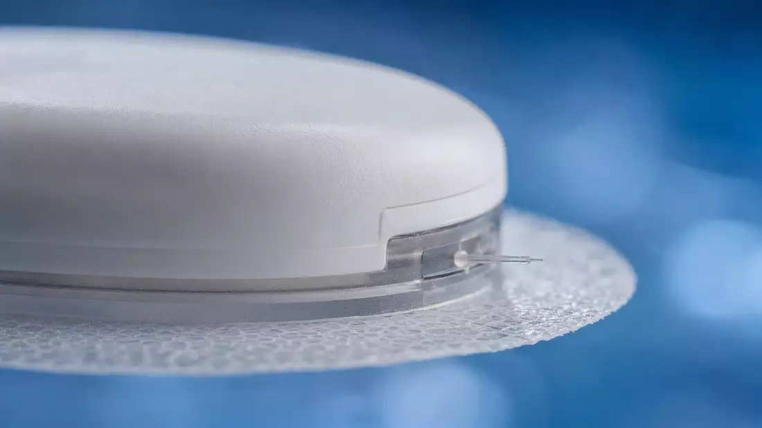 Makroaufnahme Insulet – weißer Insulin-Pod-Device mit Klebefolie und Kanüle auf blauem Bokeh