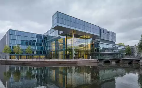 ING Groep N.V. Bankzentrale NL0011821202 als modernes Glasgebäude am Amsterdamer Kanal bei bewölktem Himmel - Foto: THN