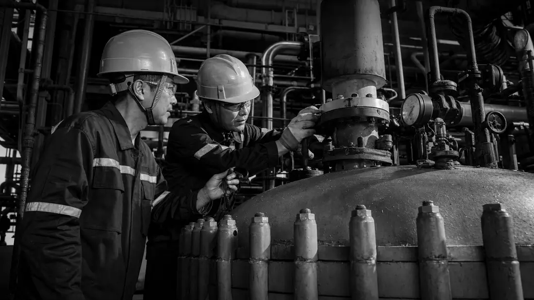 Schwarzweiß-Reportagefoto zweier Industriearbeiter beim Prüfen eines chemischen Reaktors