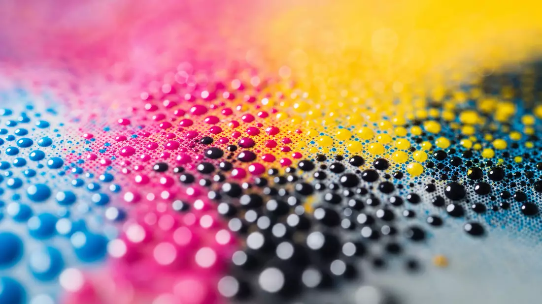 Extreme Makroaufnahme bunter CMYK-Tintentropfen auf glänzender Fotopapieroberfläche