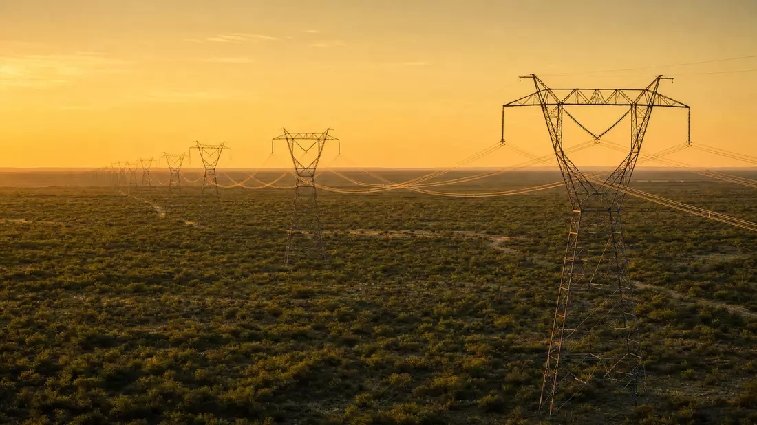 Luftaufnahme von Hochspannungsmasten auf texanischer Prärie bei goldenem Abendlicht