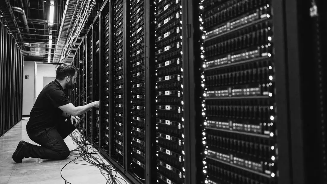 Dokumentarische Schwarzweißaufnahme eines Technikers an Server-Racks im Rechenzentrum