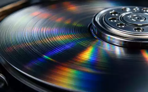 Seagate Technology (IE00B58PMW19): extreme Makroaufnahme einer magnetischen Festplatten-Oberfläche mit schillernden, regenbogenfarbenen Lichtreflexen und feinen Rillen - Foto: THN