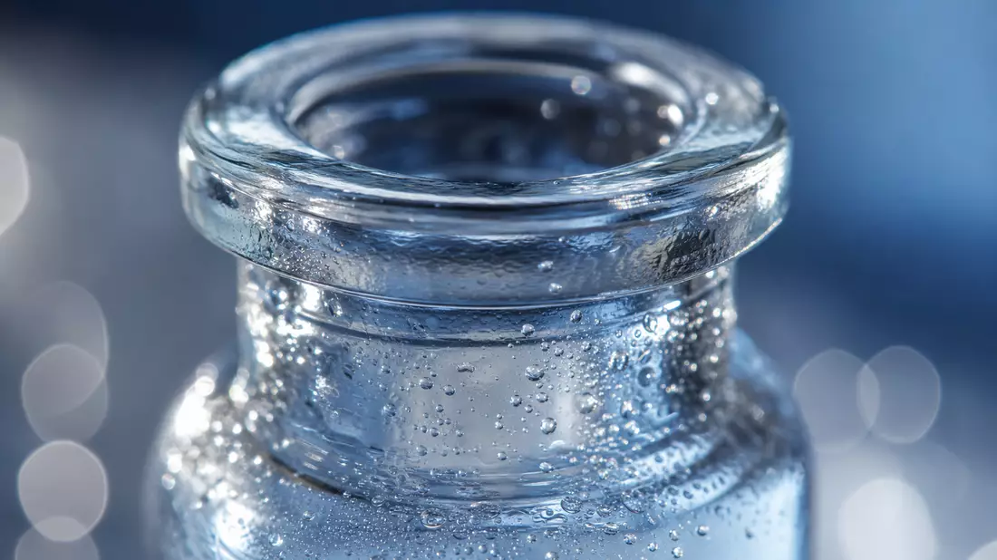 Makroaufnahme des Glasrands eines Pharma-Fläschchens mit Wassertropfen