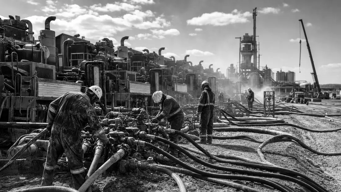 Schwarzweiß-Dokumentarfoto einer Fracking-Anlage mit arbeitendem Servicepersonal