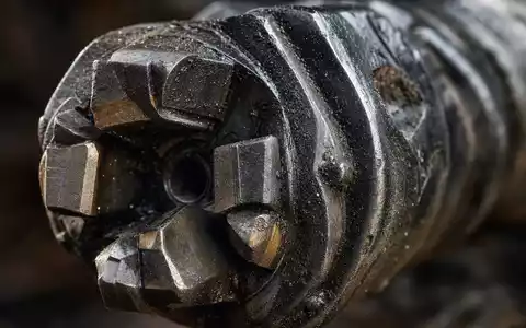 Schlumberger NV Makroaufnahme eines Bohrkopfs mit Hartmetall-Schneiden, ISIN US06520E1029, Detailansicht mit Gesteinsstaub - Foto: THN