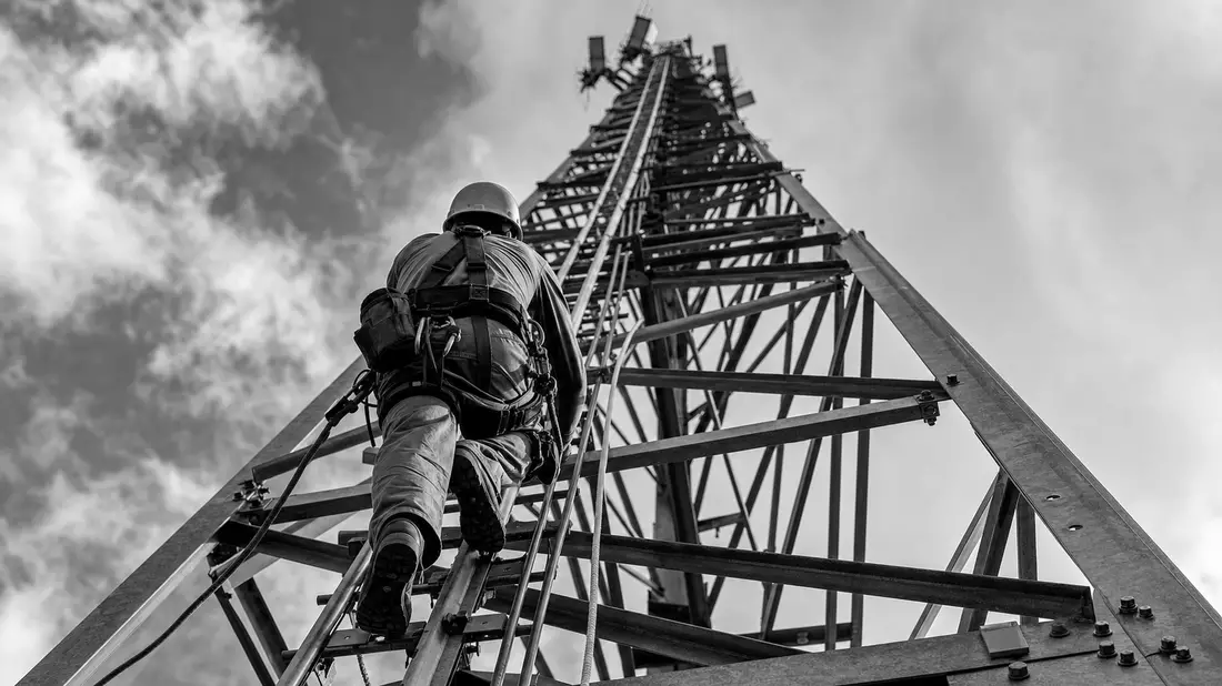 Schwarzweiß-Aufnahme eines Technikers beim Klettern auf einem Stahlgitter-Funkturm