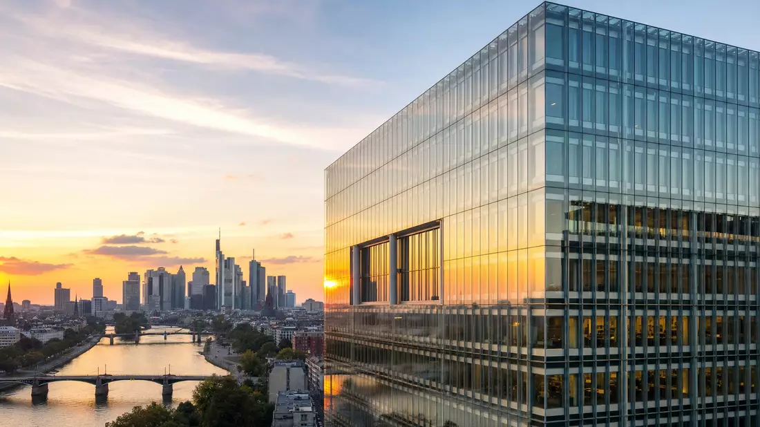 Glasfassade eines Bankhochhauses in Frankfurt bei Sonnenuntergang mit Skyline im Hintergrund