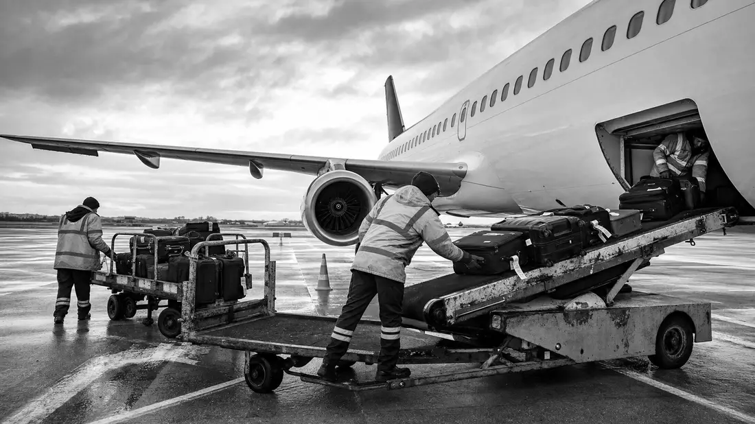Schwarzweißfoto von Bodenpersonal beim Gepäckverladen am Flugzeug
