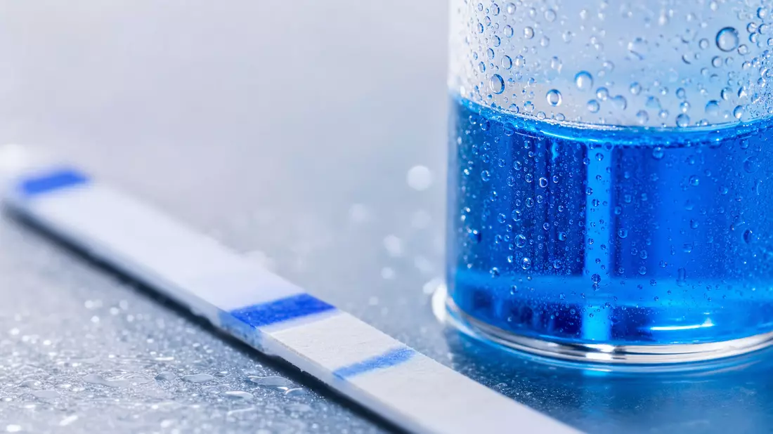 Extreme Nahaufnahme eines Teststreifens und Reagenzglases mit blauer Flüssigkeit