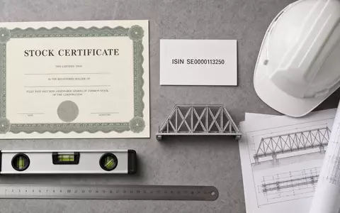 Skanska AB (SE0000113250) zeigt als Flatlay Aktienzertifikat, ISIN-Karte, Bauhelm und Brückenmodell arrangiert - Foto: THN