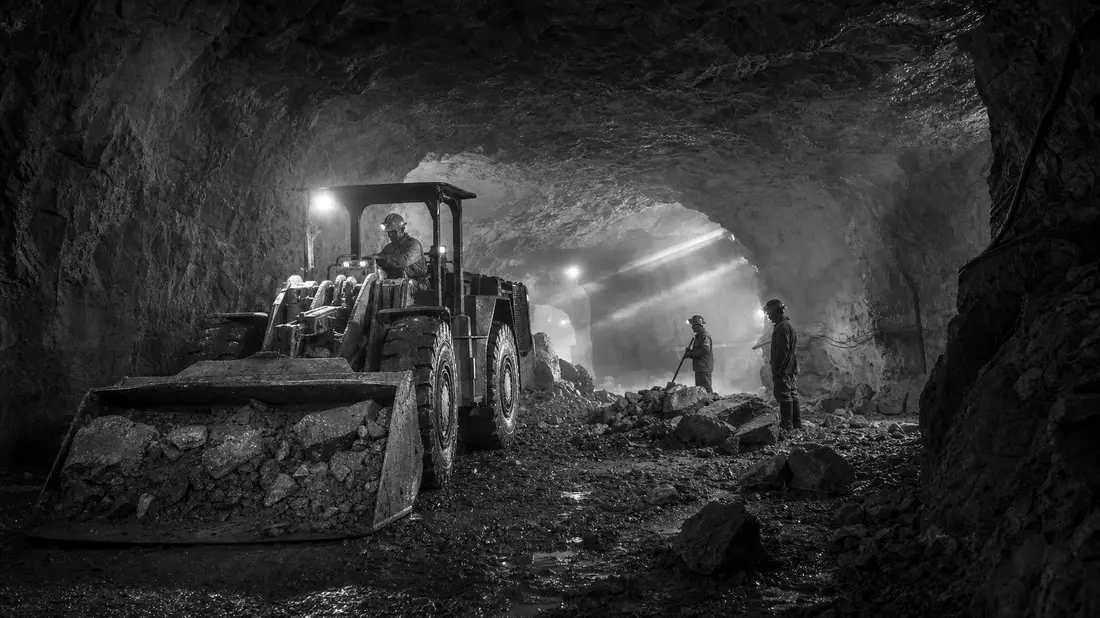 Schwarzweiß-Reportagefoto von Bergarbeitern und Lader in einem Minentunnel