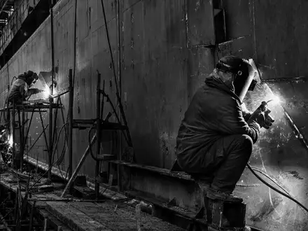 Huntington Ingalls Schweißer arbeiten in Schwarzweiß an einem massiven Schiffsrumpf in der Werft US4464131063 - Foto: THN