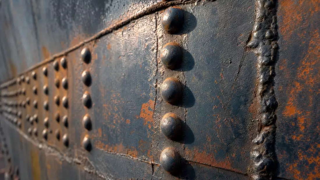 Extremes Makro-Detail: Verniettete Schiffsstahlplatten mit Schweißnähten, Rost und Farbschichten