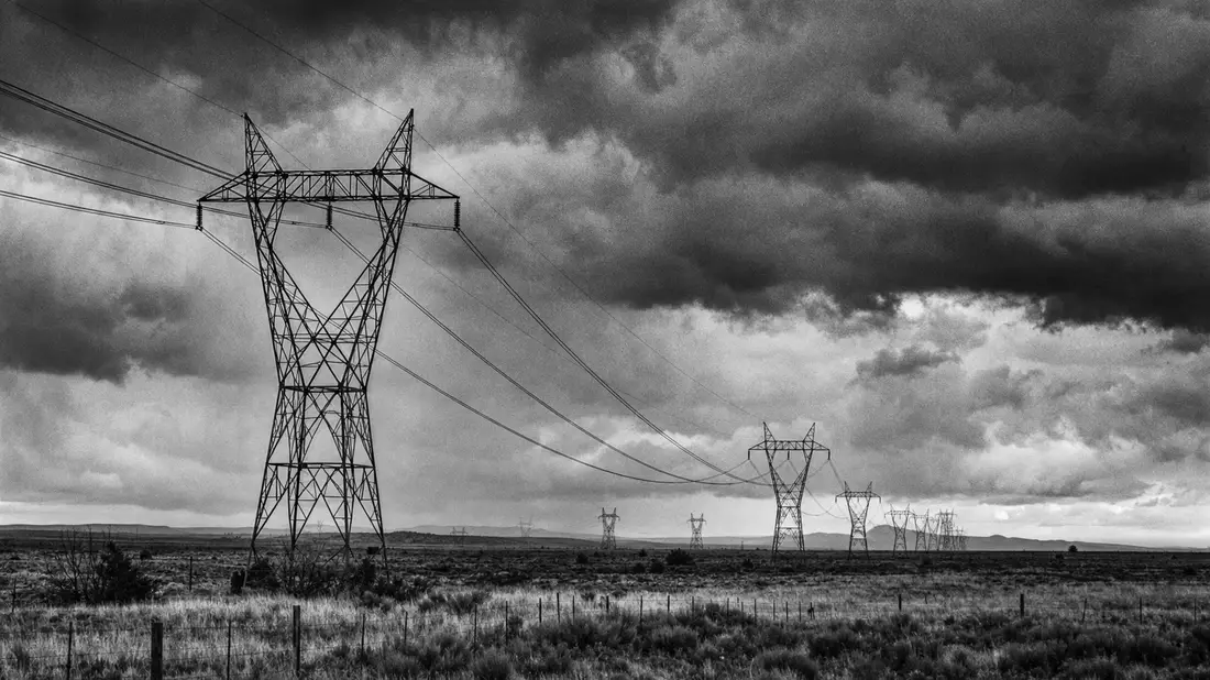 Schwarzweiß-Reportage von Hochspannungsmasten unter Gewitterhimmel