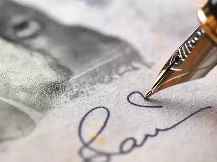 Makroaufnahme von Banknotenpapier und Füllfeder symbolisiert Finanzgeschäfte von M&G plc, ISIN GB00B03MM408 - Foto: THN