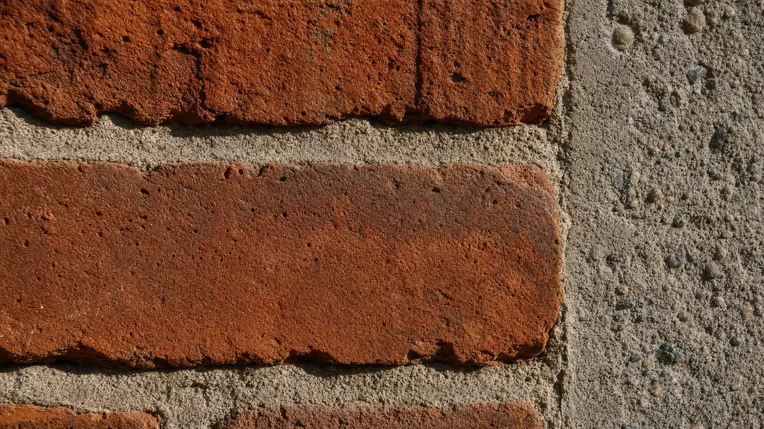 Extreme Nahaufnahme von rotem Backstein neben strukturierter Betonoberfläche