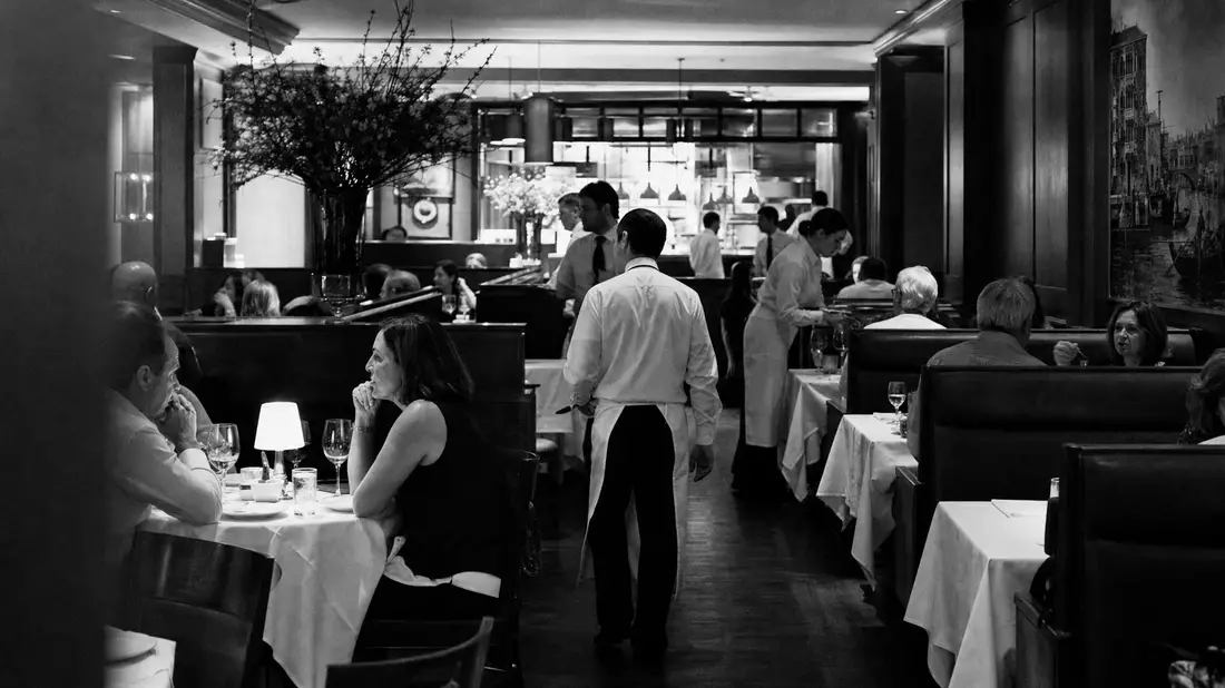 Schwarz-Weiß-Reportagefoto eines belebten Restaurantsaals mit Servicepersonal
