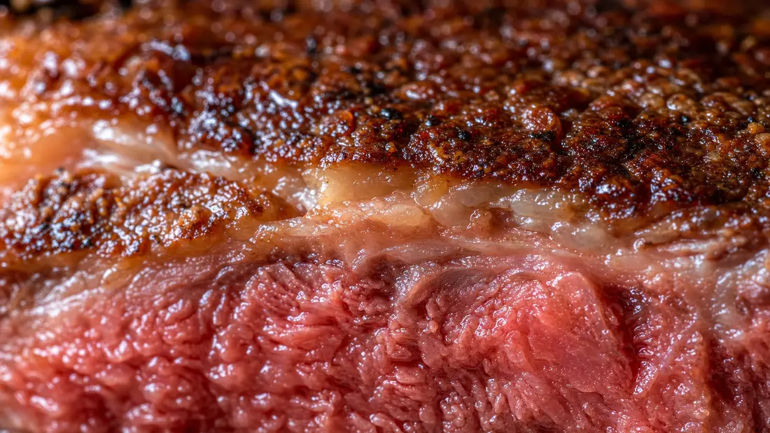 Extremes Makrofoto der Kruste eines gegrillten Rindersteaks mit sichtbarer Marmorierung und Röstaromen