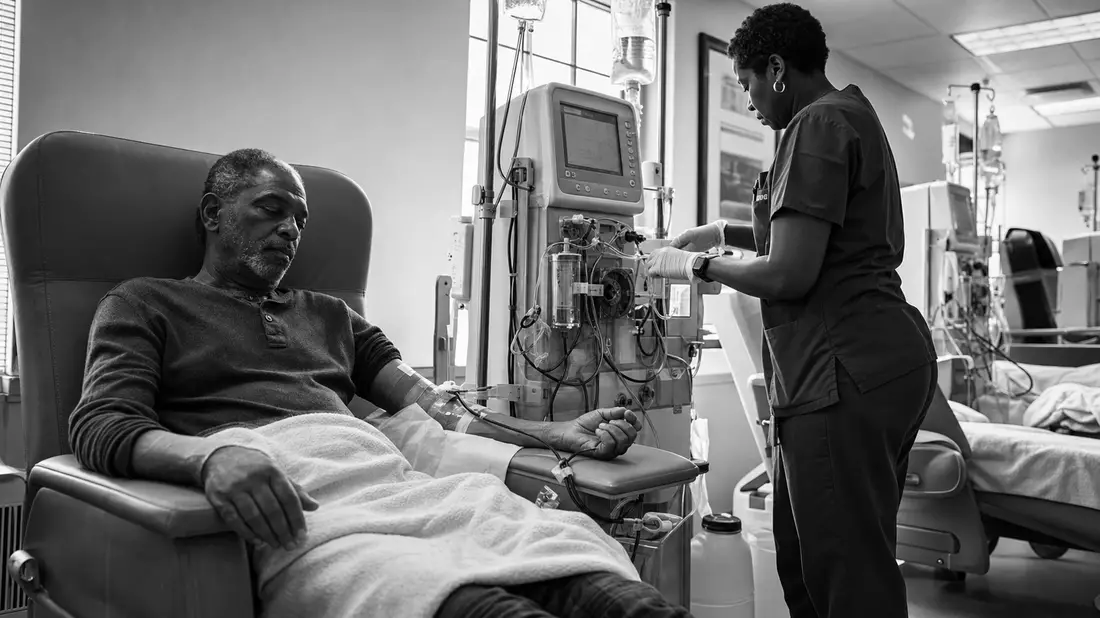 Schwarzweiß-Reportagefoto eines Dialysepatienten mit Pflegekraft in Klinikumgebung