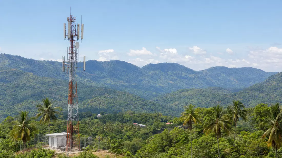 Mobilfunkmast zwischen Palmen und Bergen in tropischer Landschaft Lateinamerikas