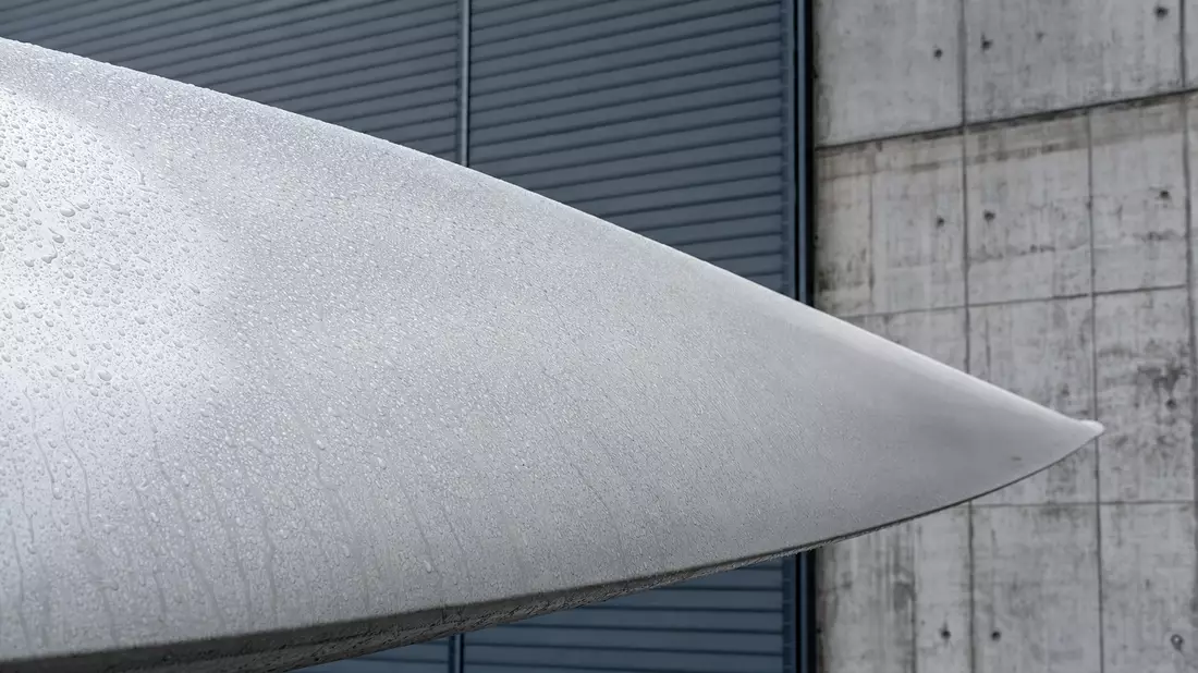 Makroaufnahme einer nassen Windturbinenschaufel vor einer Betonfassade
