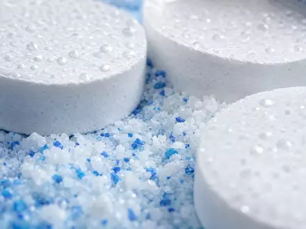 Pool Corporation US73278L1052 zeigt Makroaufnahme von weißen Chlortabletten und körnigem Poolchemikalien-Pulver mit Wassertropfen - Foto: THN