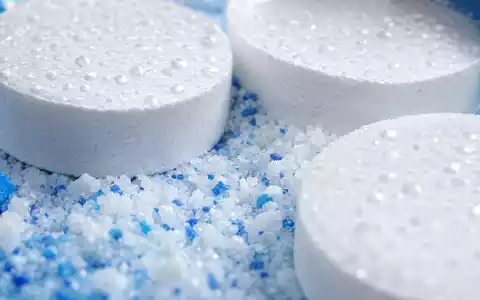 Pool Corporation US73278L1052 zeigt Makroaufnahme von weißen Chlortabletten und körnigem Poolchemikalien-Pulver mit Wassertropfen - Foto: THN