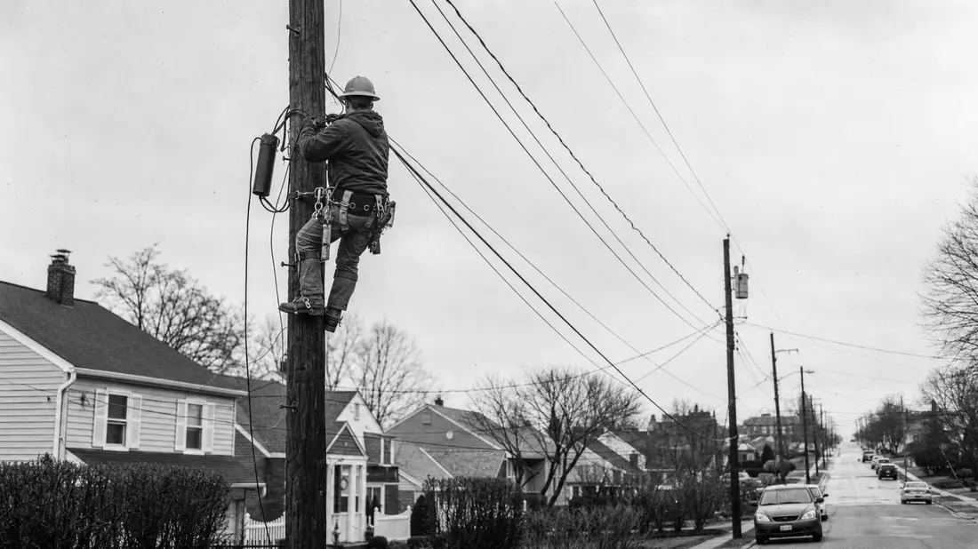 Schwarzweiß-Reportagefoto eines Kabeltechnikers auf einem Strommast in der Vorstadt