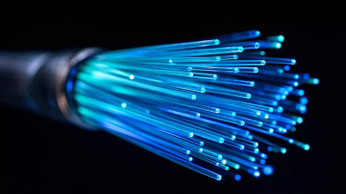 Makro-Aufnahme leuchtender Glasfaserkabel mit cyan-blauem Licht vor schwarzem Hintergrund