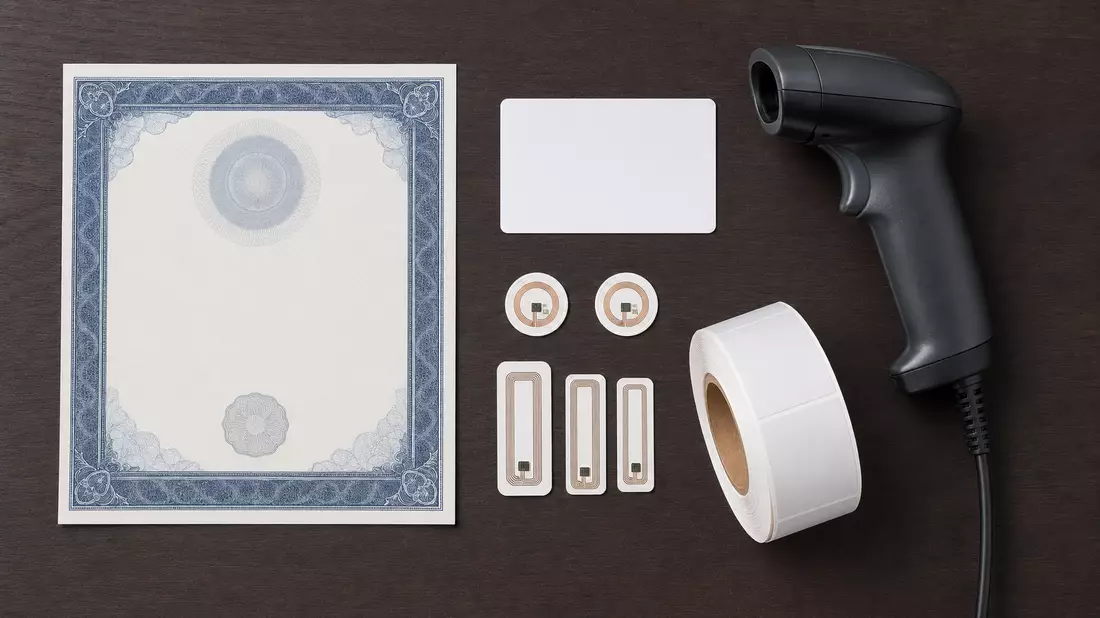 Flatlay mit Aktienzertifikat, ISIN-Karte, Handscanner, RFID-Tags und Etikettenrolle