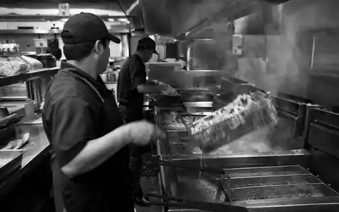Schwarzweiße Reportage-Aufnahme einer Restaurantküche zeigt Betriebsalltag von Yum! Brands Inc. ISIN US9884981013 im Fast-Food-Geschäft - Foto: THN
