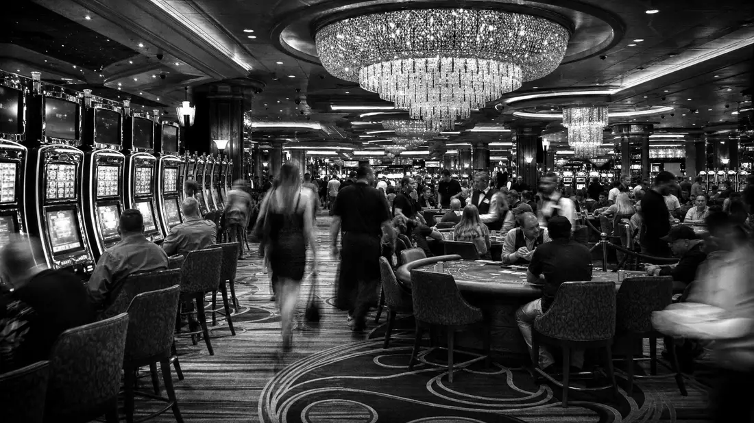 Schwarzweiß-Reportagefoto eines belebten Casino-Spielsaals mit Kronleuchtern und Gästen