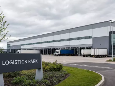 LondonMetric Property Plc GB00B4WFW713 zeigt fotorealistisches britisches Logistikzentrum mit Lkw an Verladerampen davor - Foto: THN