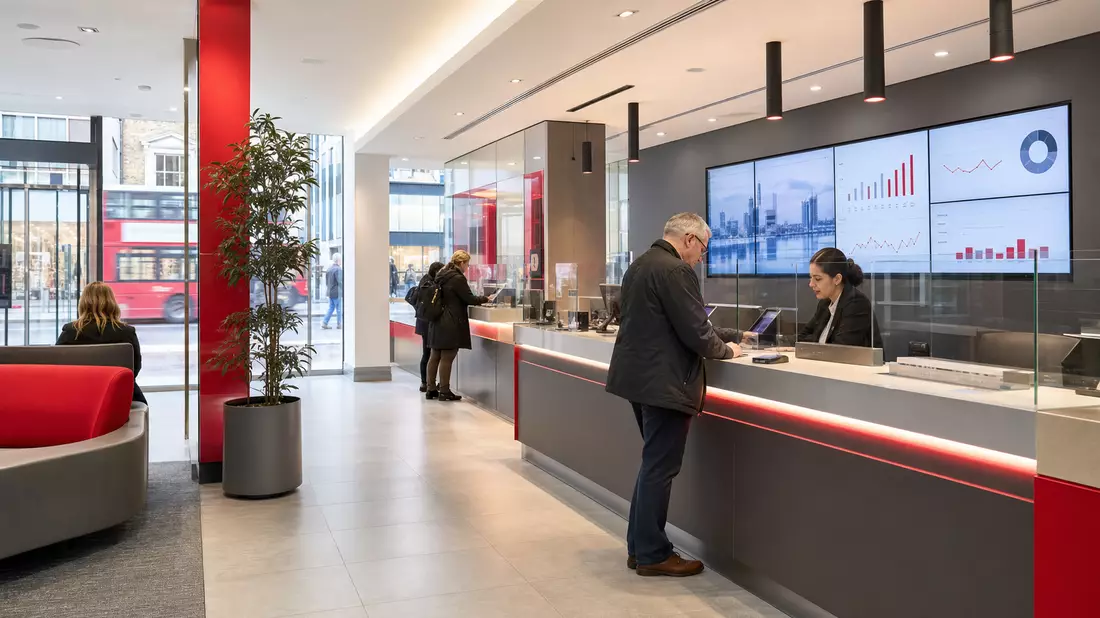 Moderne Bankfiliale mit Kundenberatung, Bildschirmen und rot-grauem Interieur