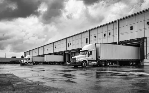 Schwarzweiß-Reportagefoto zeigt LKW an Verladerampen, passend zum Geschäft von WDP N.V., Wertpapier BE0974310428 - Foto: THN