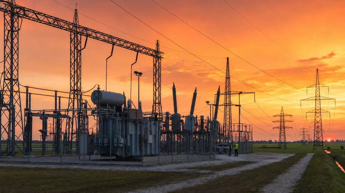 Hochspannungs-Umspannwerk bei Sonnenuntergang mit Strommasten und Technikern